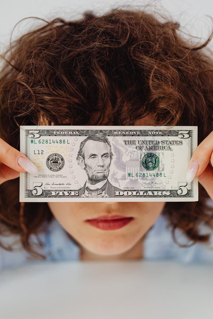 Person holding a five dollar bill close to their face with a neutral expression.